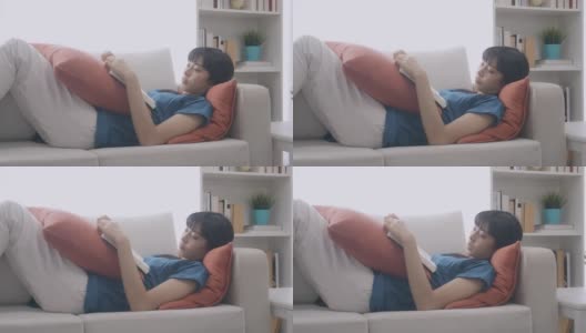 一个女人躺在沙发上看书。缓慢的运动。难过的时候,中景镜头。高清在线视频素材下载