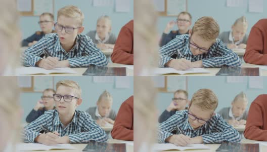 小学课堂:一个聪明的白人男孩戴着眼镜在练习本上写字。学习科学和创造性思维的多元聪明儿童群体高清在线视频素材下载