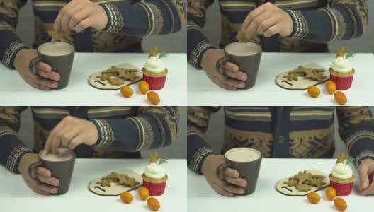 男人的手把姜饼蘸可可。桌子上有姜饼人，小蛋糕和金橘高清在线视频素材下载