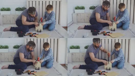 专心的孩子在用手锯锯胶合板，他的父亲用手拿着木头，帮助他的儿子教他。分享经验的概念。高清在线视频素材下载