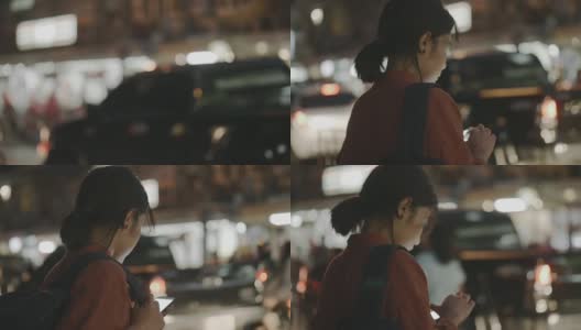一名年轻女子站在街上，一边等出租车一边看手机。——股票视频高清在线视频素材下载
