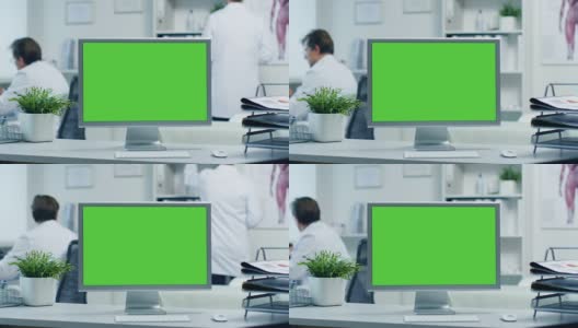 一个绿色屏幕显示器的特写。医生使用文件夹工作，助手通过电话与病人交谈。拍摄于一个明亮和现代的医生的办公室。高清在线视频素材下载