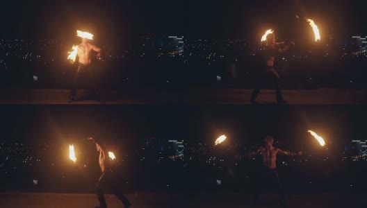 年轻的金发男子用两个火把跳火舞，在午夜与城市的天际线旋转火把高清在线视频素材下载