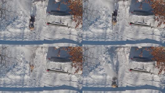 一名成年男子在一场冬季降雪后用除雪机清理车道上的积雪。鸟瞰图正上方无人机视频。高清在线视频素材下载