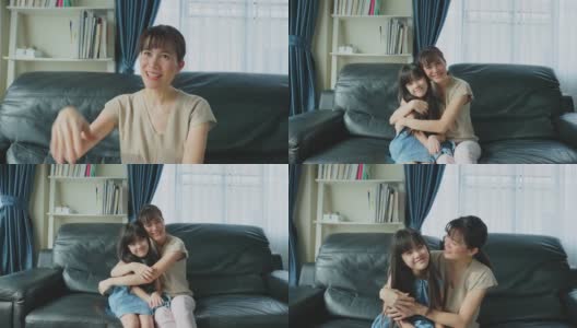 亚洲幸福家庭，父母在家里和孩子一起度过空闲时间。快乐的小女儿和妈妈坐在客厅的沙发上，微笑着看着摄像机。活动关系在房子概念高清在线视频素材下载