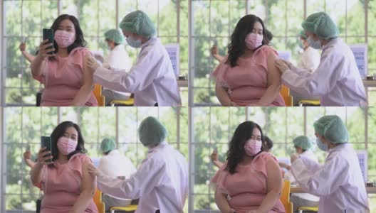 图为一名亚洲女性在诊所或医院接种新冠疫苗时的自拍照片，护工正在注射疫苗以获得保护病毒的免疫力。人们戴着防护口罩。高清在线视频素材下载