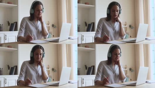 戴着耳机的年轻女性在电脑屏幕前做笔记高清在线视频素材下载