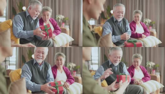 年轻的亚洲男性儿子在家中客厅交谈并把圣诞礼物盒送给祖父母，年老的亚洲退休夫妇留在家中与家人一起欢度节日高清在线视频素材下载