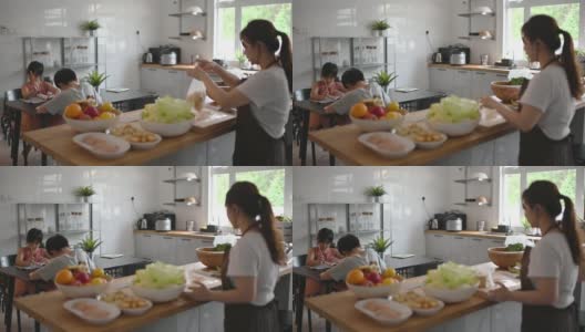 两个孩子在家学习写中国书法，而他们的母亲在厨房柜台准备食物高清在线视频素材下载