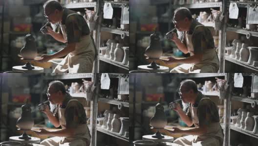 亚洲华人高级泥塑艺术家在雕塑家身上吹颜料，在他的工作室里用纺纱陶轮工作高清在线视频素材下载