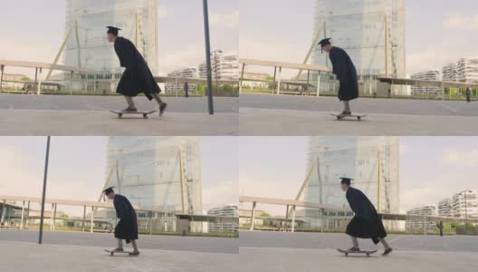 一名大学生刚毕业，穿着毕业生长袍玩滑板，在市中心的高楼大厦之间表演特技。高清在线视频素材下载