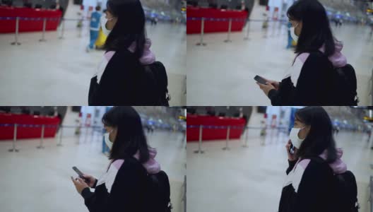 亚洲女性在机场航站楼主厅使用智能手机佩戴医用口罩，旅行导航系统应用，新冠肺炎大流行后，新常态社会距离概念，慢动作高清在线视频素材下载