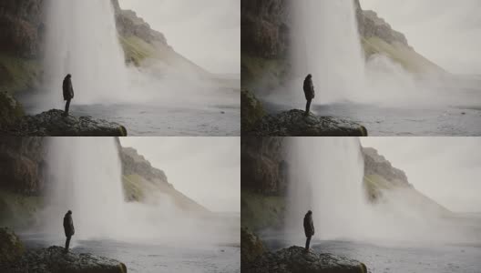 一名年轻男子带着摄像机站在冰岛的Gljufrabui瀑布附近，拍摄水流的视频高清在线视频素材下载