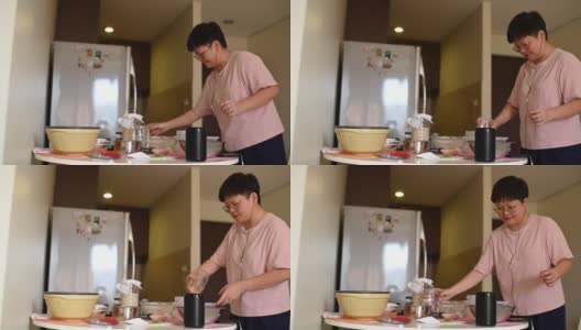一位亚洲华人家庭妈妈在准备面团的同时，使用虚拟助手智能音箱来制作食谱和指导高清在线视频素材下载