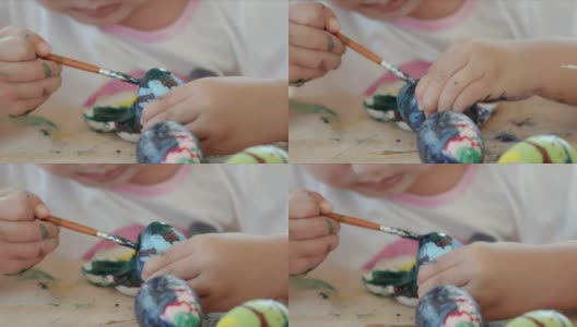小女孩在书桌上用画笔和颜料给复活节彩蛋涂色。高清在线视频素材下载