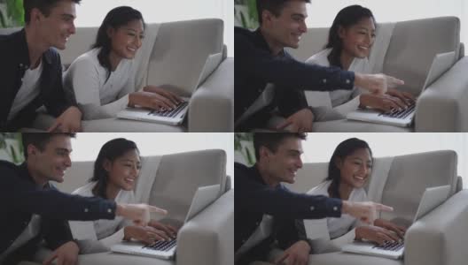 一对年轻夫妇在沙发上悠闲地摆弄着笔记本电脑高清在线视频素材下载