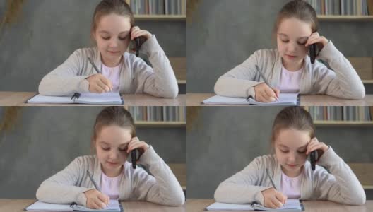 一个女学生坐在家里的桌子边打电话，在笔记本上做笔记。高清在线视频素材下载