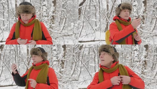 一名年长的白人男子穿过冬季森林，试图通过智能手机捕捉信号。密密麻麻的树木和树根在白雪皑皑的森林里。远足和旅行概念60帧/秒高清在线视频素材下载