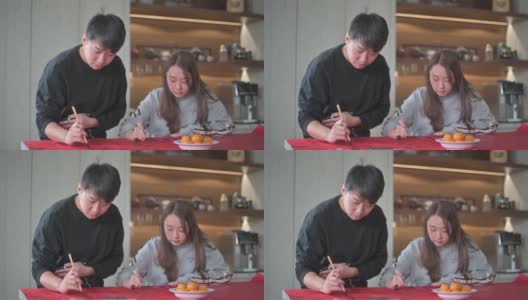 亚洲华人家庭在红纸上书写中国书法，以求繁荣，准备中国新年的家庭装饰高清在线视频素材下载