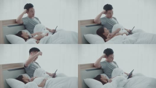 亚洲可爱的已婚年轻夫妇醒来在他们的卧室，使用平板电脑看电影，在睡觉前幸福在一起，4K分辨率，人类关系概念。高清在线视频素材下载