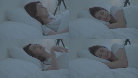 亚洲美丽舒适的女孩穿着睡衣睡在黑暗的夜晚在卧室。漂亮的年轻女子躺在床上，感觉幸福与舒适的枕头和毯子，做一个好梦，微笑在家里。高清在线视频素材下载