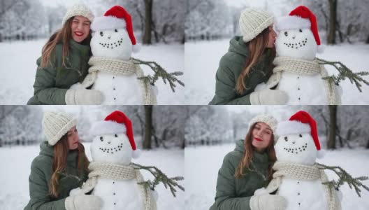 在下雪的冬天公园里，女人戴着圣诞帽和围巾亲吻雪人。圣诞节的庆祝活动。户外活动高清在线视频素材下载