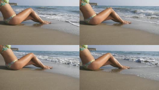 海浪冲刷着年轻女性的脚。难以辨认的迷人的女人在比基尼躺在海滩上。晒黑的女孩在美丽的海岸晒太阳。暑假或假日概念。关闭慢动作侧视图低角度视图高清在线视频素材下载
