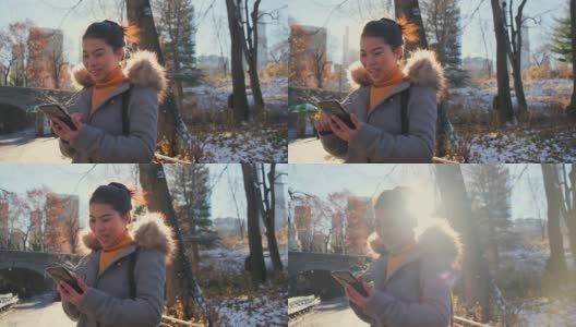 年轻的亚洲女性穿着冬衣微笑享受和平漫步在中央公园的冬季和黄色的树与地面的雪秋天手用智能手机设备的旅游概念高清在线视频素材下载