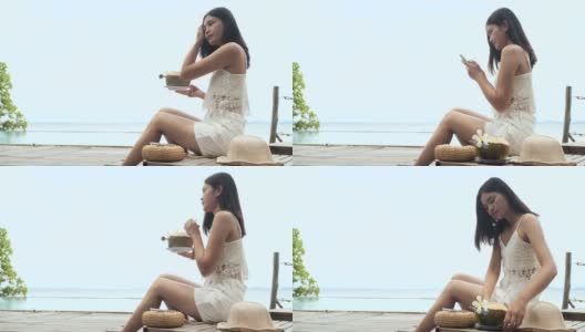 美丽年轻的亚洲女人喝椰子汁沿着海滩。高清在线视频素材下载