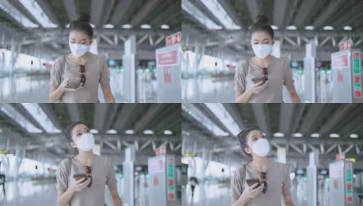 年轻迷人的亚洲女性旅行者戴着口罩，手拿智能手机，查看地图和航班时刻表，在机场航站楼拿着行李和手提包醒来，新的旅行生活方式高清在线视频素材下载