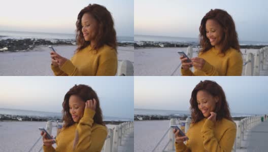 微笑的非裔美国女性在海滩上使用智能手机高清在线视频素材下载