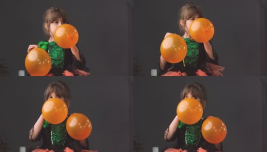 一个漂亮的小女孩穿着漂亮的裙子，嘴巴握在手里，为万圣节派对依次吹着橙色的气球。高清在线视频素材下载