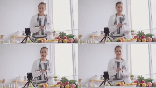 亚洲资深女性作为影响者，教如何制作自制的水果冰沙与不同的口味和酸奶。健康天然益生菌调味饮料，学会使用科技，在厨房用智能手机与观众交谈，低角度高清在线视频素材下载