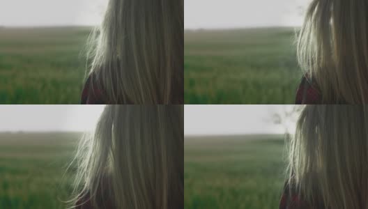 黄昏或黎明时分，一个年轻浪漫的女孩身穿红色格子衬衫站在田野里。头发被风吹着高清在线视频素材下载