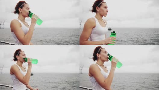 口渴的健身妇女休息休息，用水瓶饮用训练后。在海边训练的美女高清在线视频素材下载