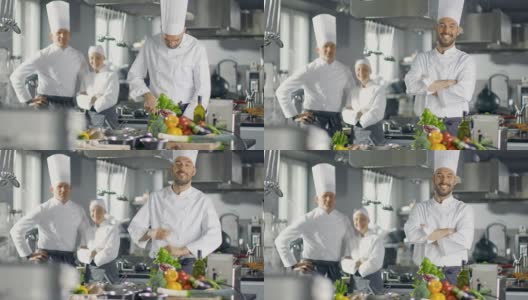 一家大餐厅的著名厨师在现代厨房里双臂交叉微笑。他的员工在背后微笑。高清在线视频素材下载