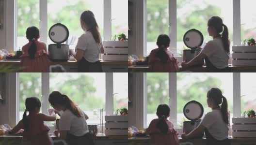 亚洲华人妈妈在厨房做饭，她的女儿用电饭煲煮米饭高清在线视频素材下载