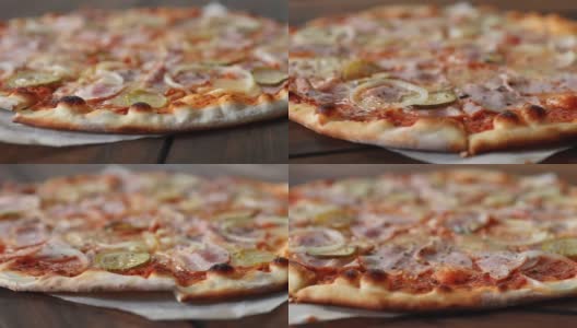 新鲜的圆形披萨，配上马苏里拉奶酪、意大利腊肠、黄瓜和洋葱，在棕色木桌上近距离从左到右旋转。披萨店的美味快餐背景高清在线视频素材下载