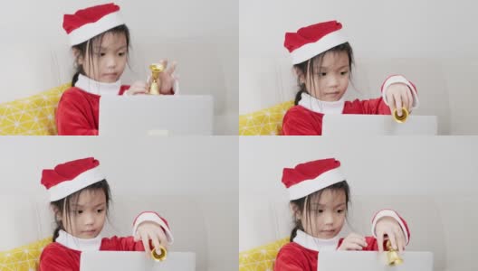 快乐的亚洲女孩穿着圣诞老人服装，坐在家里的沙发上，生活理念。高清在线视频素材下载