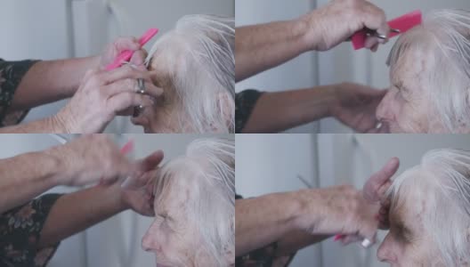 一个专业护理发型师在剪一个年长的白人妇女的刘海期间在家理发的近距离手持式拍摄高清在线视频素材下载