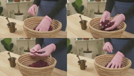 一个戴着粉色手套的女孩整理着干玫瑰花瓣。篮子里装满了干花。创造天然手工化妆品的过程。高清在线视频素材下载