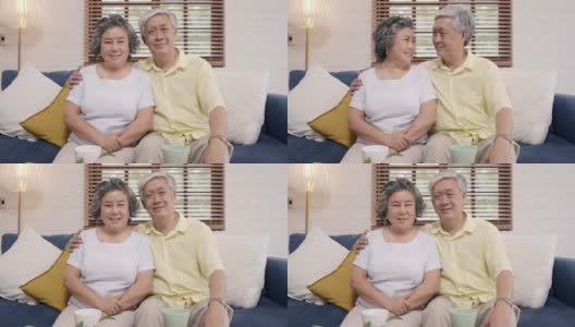 一对亚洲老夫妇在家里客厅的沙发上放松时，开心地微笑着，看着镜头。享受时光的生活方式高级家庭在家里的概念。看着相机的人像。高清在线视频素材下载