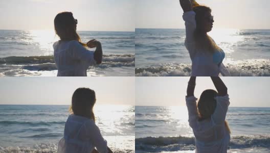 穿着比基尼和衬衫的年轻女子在海岸上旋转，并举起她的手。美丽的金发女孩沿着海边散步，享受生活。暑假放松一下。特写慢动作侧视图高清在线视频素材下载