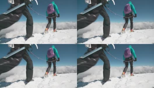 两名女性登山运动员在云层之上的高海拔处，在风吹过的冰川上穿越山脊。高清在线视频素材下载
