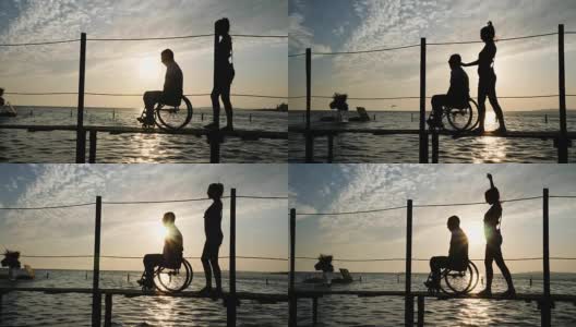瘦弱的女孩和坐轮椅的残疾人在夕阳下的海上码头上行走高清在线视频素材下载