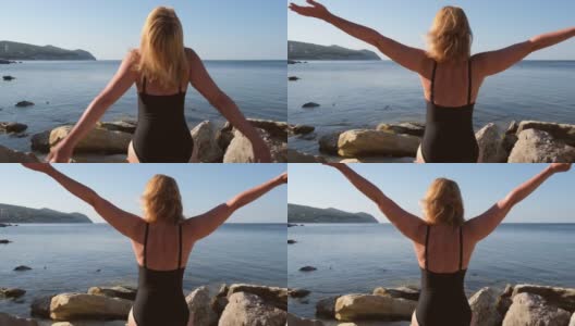 日出时，一个金发女人在海滩上张开双臂。快乐的女孩享受生活在黑色的泳装清晨在海滨。运动和健康的生活方式。生命，治愈和自由的概念高清在线视频素材下载