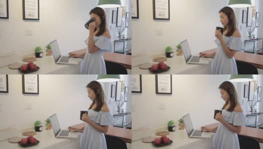 一名亚裔中国妇女在家喝咖啡时用笔记本电脑工作高清在线视频素材下载