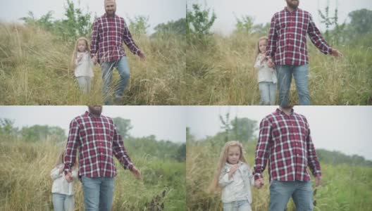 可爱的白种人小女孩和满脸胡须的年轻男子在户外秋天的草地上散步。漂亮的女儿牵着爸爸的手散步，四处张望。高清在线视频素材下载