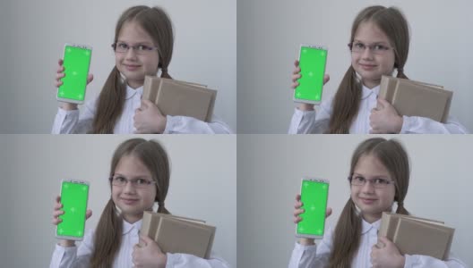 一名女学生，穿着白色的校服，戴着眼镜，拿着书，拿着绿屏手机。绿屏智能手机的色度键设置为广告。教育、科技、小玩意和孩子高清在线视频素材下载