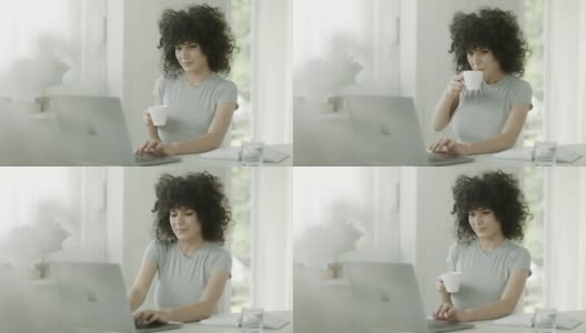 年轻女子端着咖啡在办公室使用笔记本电脑高清在线视频素材下载